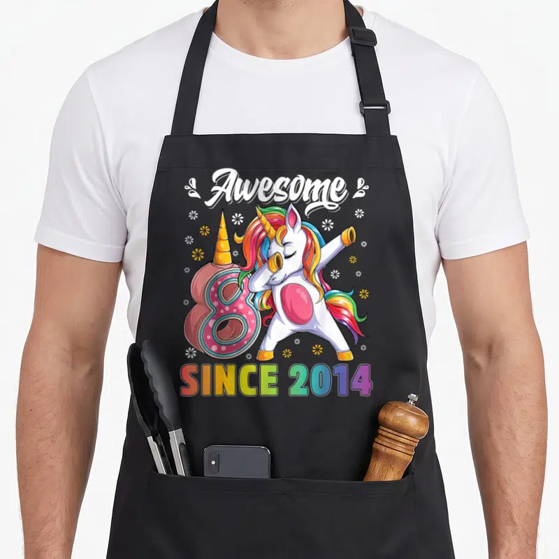 Dabbing unicorn 8th birthday apron - Cartoon unicorn dabbing next to pink number 8 with since 2014 rainbow text — shown on a black cotton canvas apron against a white background