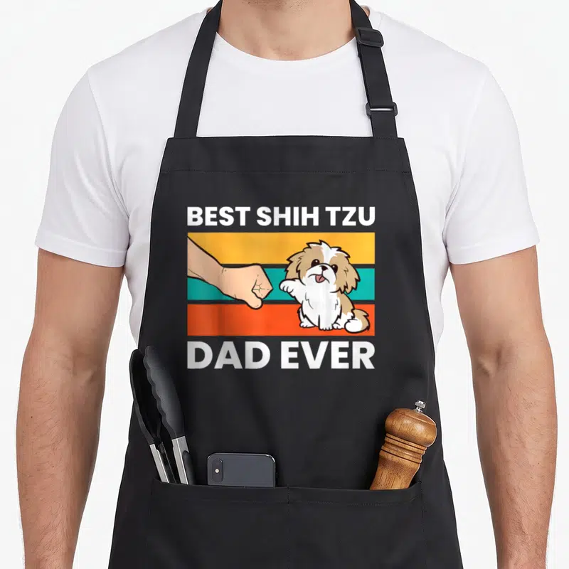 Funny shih tzu apron - Cartoon shih tzu fist bumping a human hand over three colored stripes with best shih tzu dad — shown on a black cotton canvas apron against a white background
