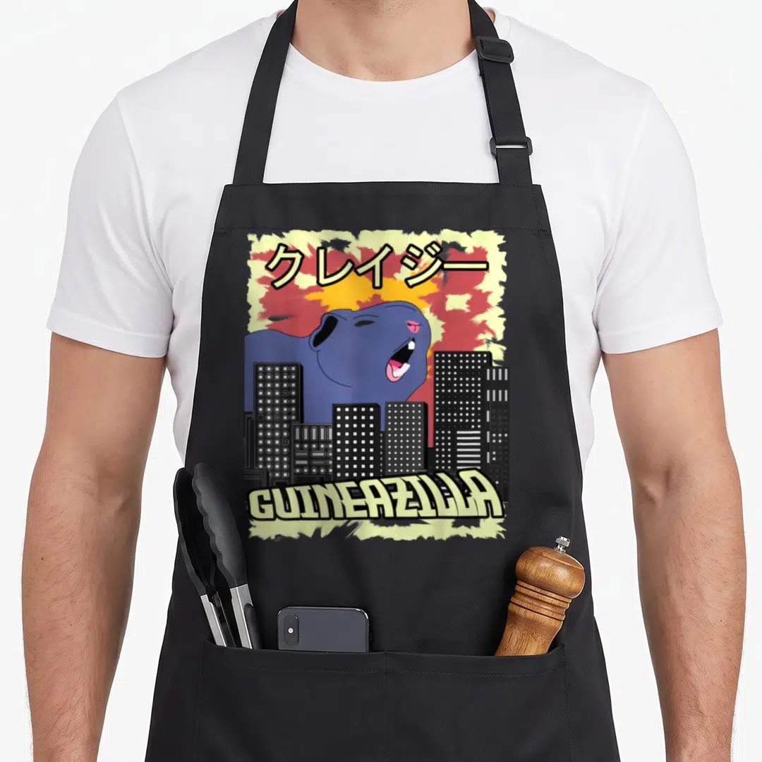 Loco japan apron - Blue guinea pig monster towering over city buildings with Katakana text and Guineazilla label — shown on a black cotton canvas apron against a white background