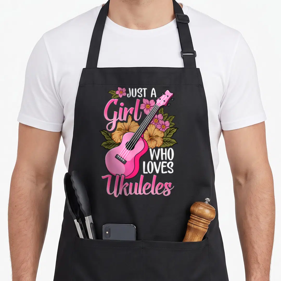 Funny ukulele lover apron - Pink ukulele angled diagonally through orange and green flowers with text JUST A Girl WHO — shown on a black cotton canvas apron against a white background