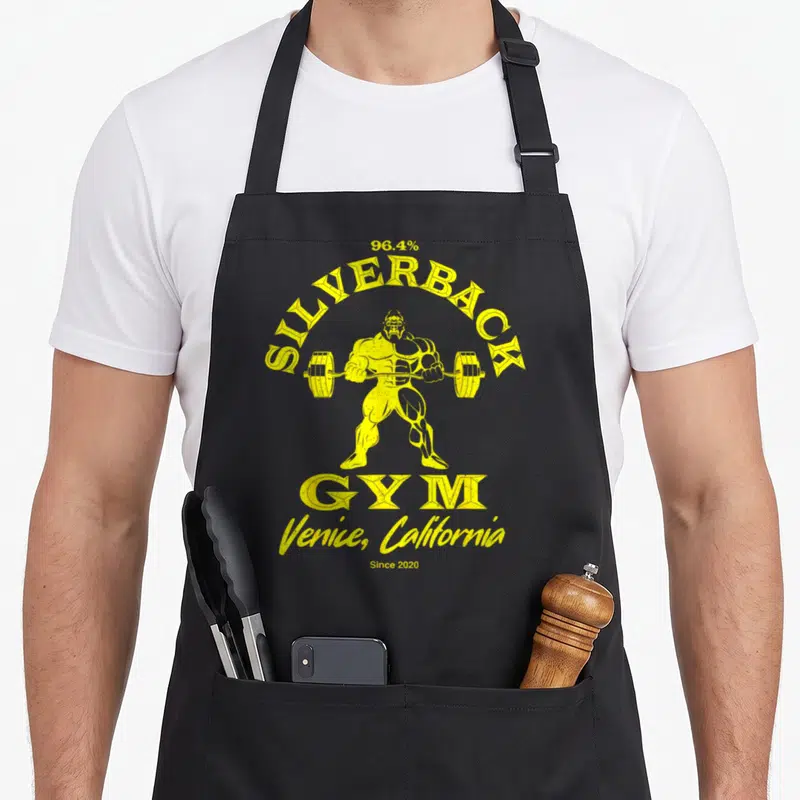 Venice silverback aprons - Yellow distressed gorilla lifting barbell with 96.4% Silverback Gym text — shown on a black cotton canvas apron against a white background