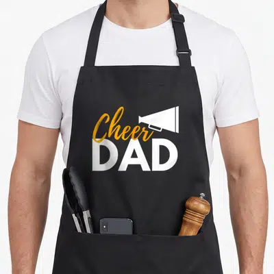 Cheer cheerleader cheerleading apron - Orange script Cheer and white DAD text with a white megaphone icon — shown on a black cotton canvas apron against a white background
