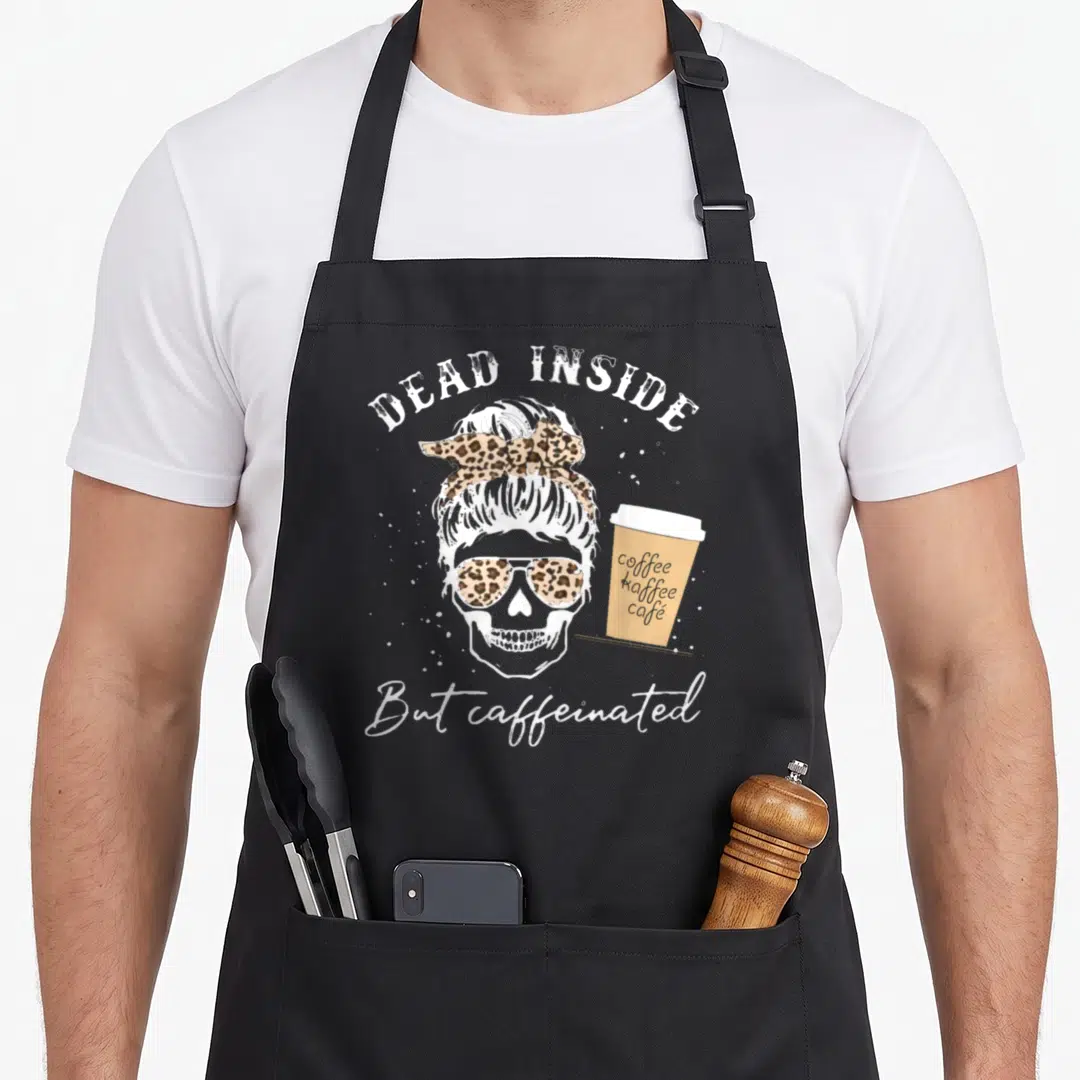 Skull messy aprons - Skeleton with leopard bun sunglasses holding coffee cup reading dead inside but caffeinated — shown on a black cotton canvas apron against a white background
