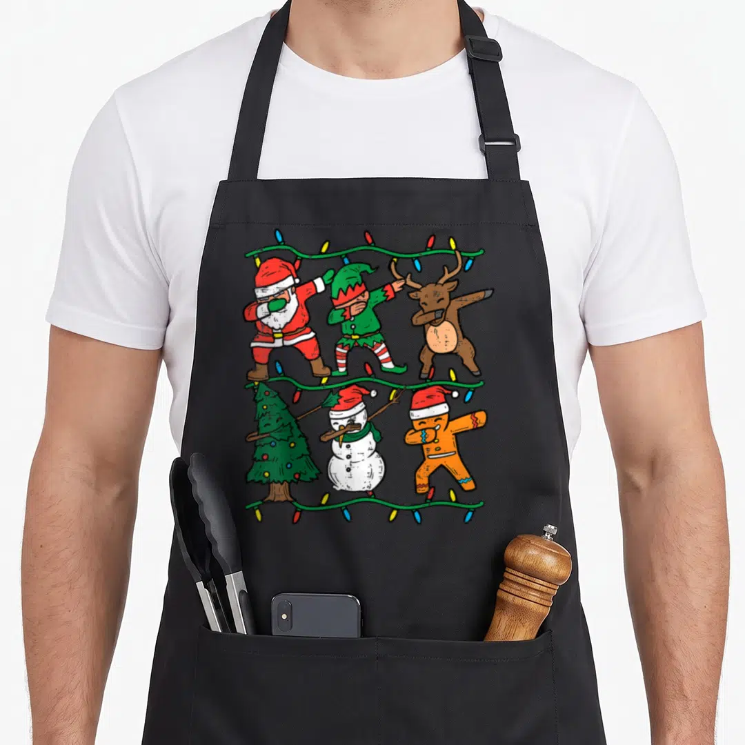 Pjs christmas elf apron - Six dabbing Christmas characters including Santa, elf, reindeer, tree, snowman — shown on a black cotton canvas apron against a white background