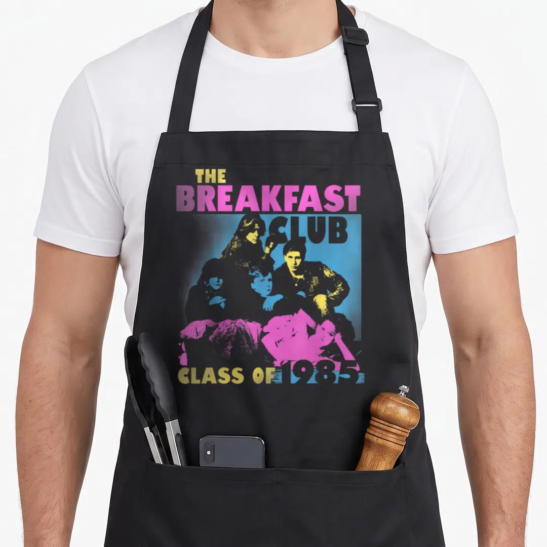 Class breakfast apron - Five people in pink blue yellow with The Breakfast Club Class of 1985 text — shown on a black cotton canvas apron against a white background