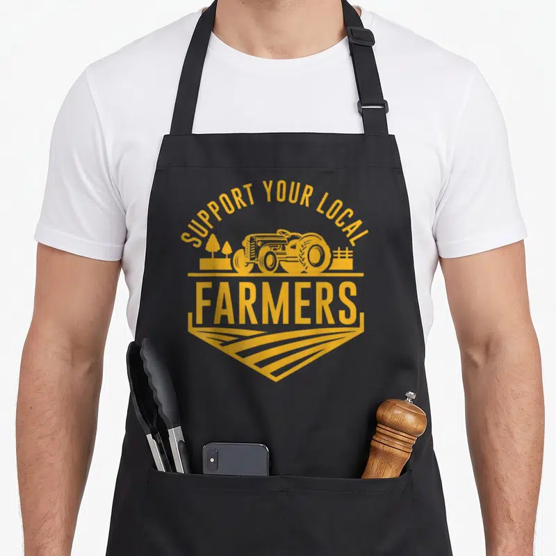 Local farm apron - Yellow tractor and SUPPORT YOUR LOCAL FARMERS text on canvas — shown on a black cotton canvas apron against a white background