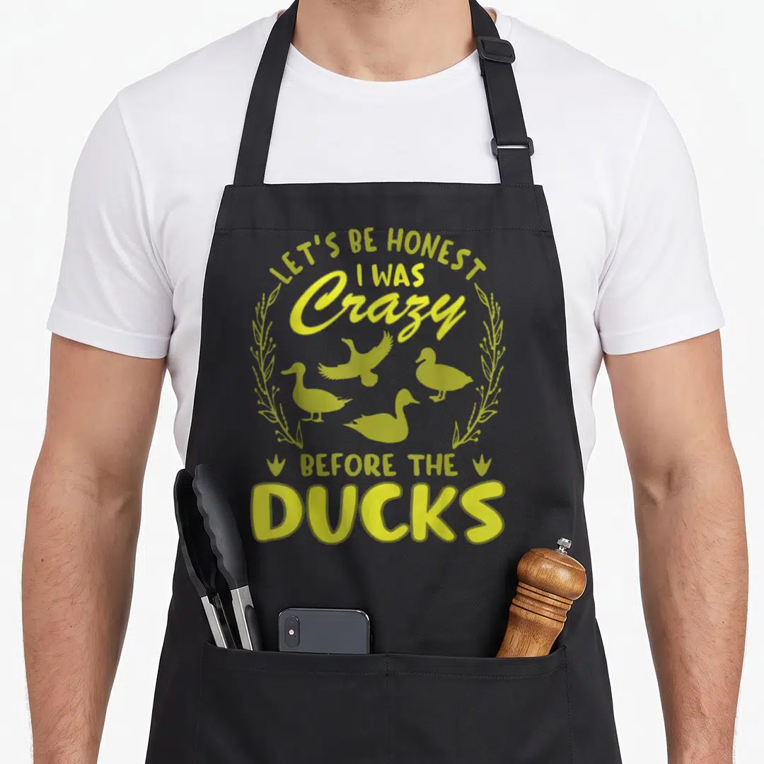Honest cotton duck aprons - Yellow typography reading Lets Be Honest I Was Crazy Before Ducks with four duck — shown on a black cotton canvas apron against a white background