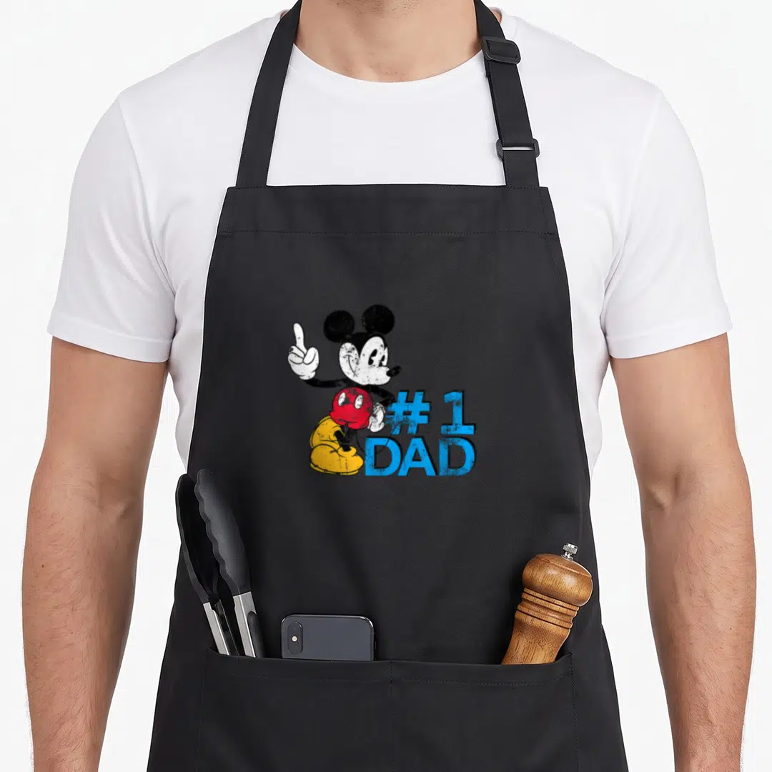 Retro father day apron - Mickey Mouse pointing up beside blue #1 DAD text in distressed colors — shown on a black cotton canvas apron against a white background