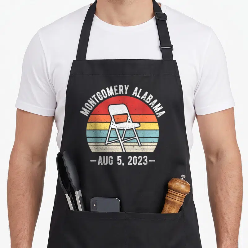 Riverfront chair apron - White folding chair on red orange yellow blue striped sun with arched text MONTGOMERY ALABAMA — shown on a black cotton canvas apron against a white background