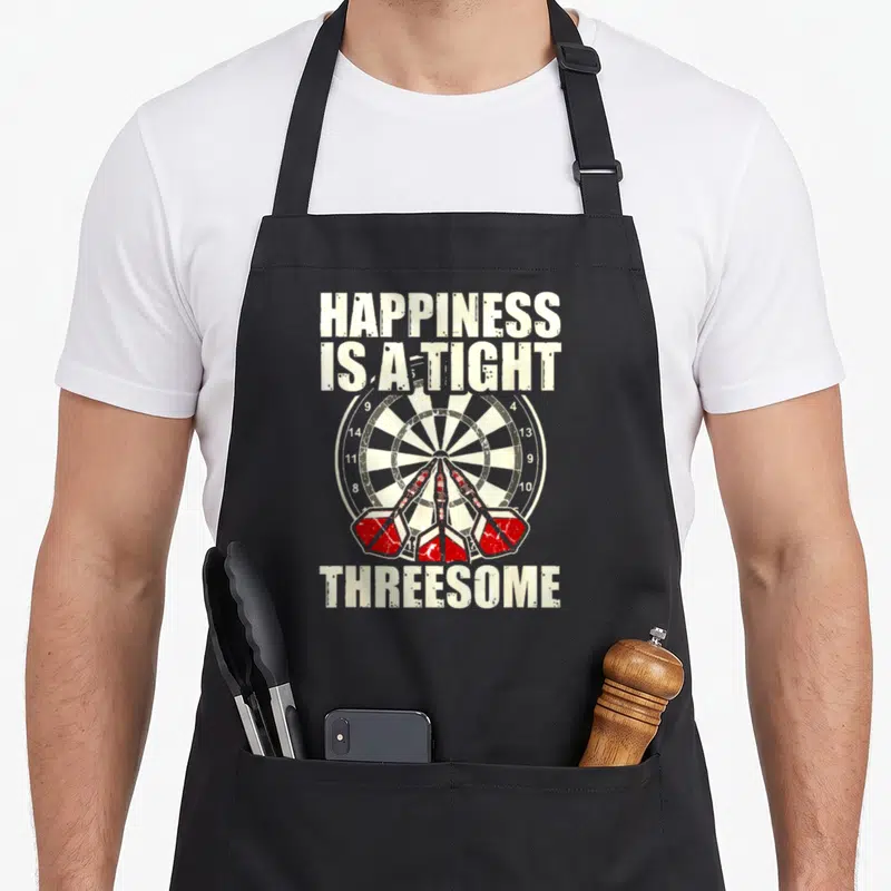 Happiness darts apron - Dartboard with three red darts and distressed text reading HAPPINESS IS A TIGHT THREESOME — shown on a black cotton canvas apron against a white background