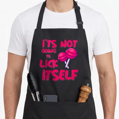 Lick candy aprons - Pink text It's Not Going to Lick Itself with two crossed cartoon lollipops — shown on a black cotton canvas apron against a white background