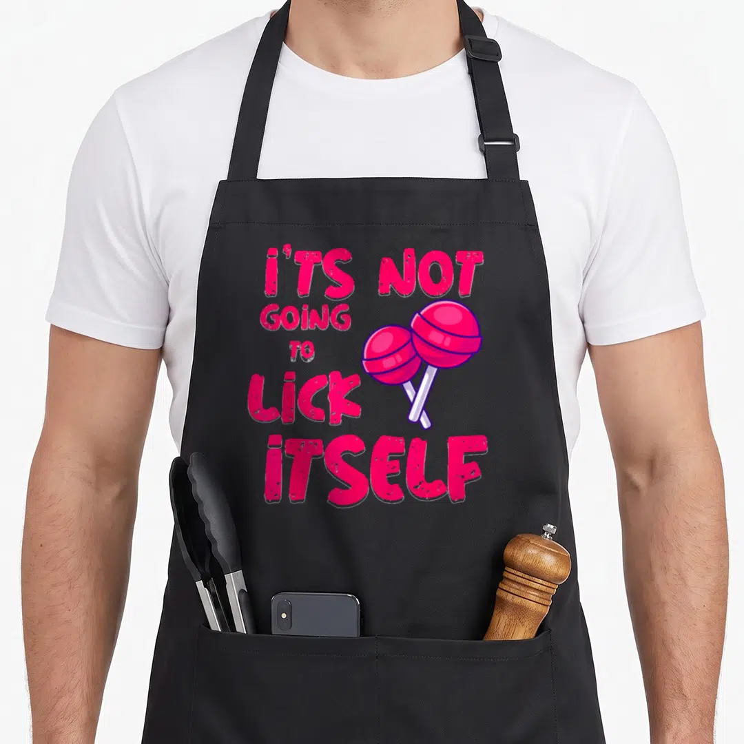 Lick candy aprons - Pink text It's Not Going to Lick Itself with two crossed cartoon lollipops — shown on a black cotton canvas apron against a white background