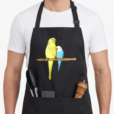 Familiy bird apron - Two cartoon parakeets perched on a brown branch with musical notes and a red heart — shown on a black cotton canvas apron against a white background