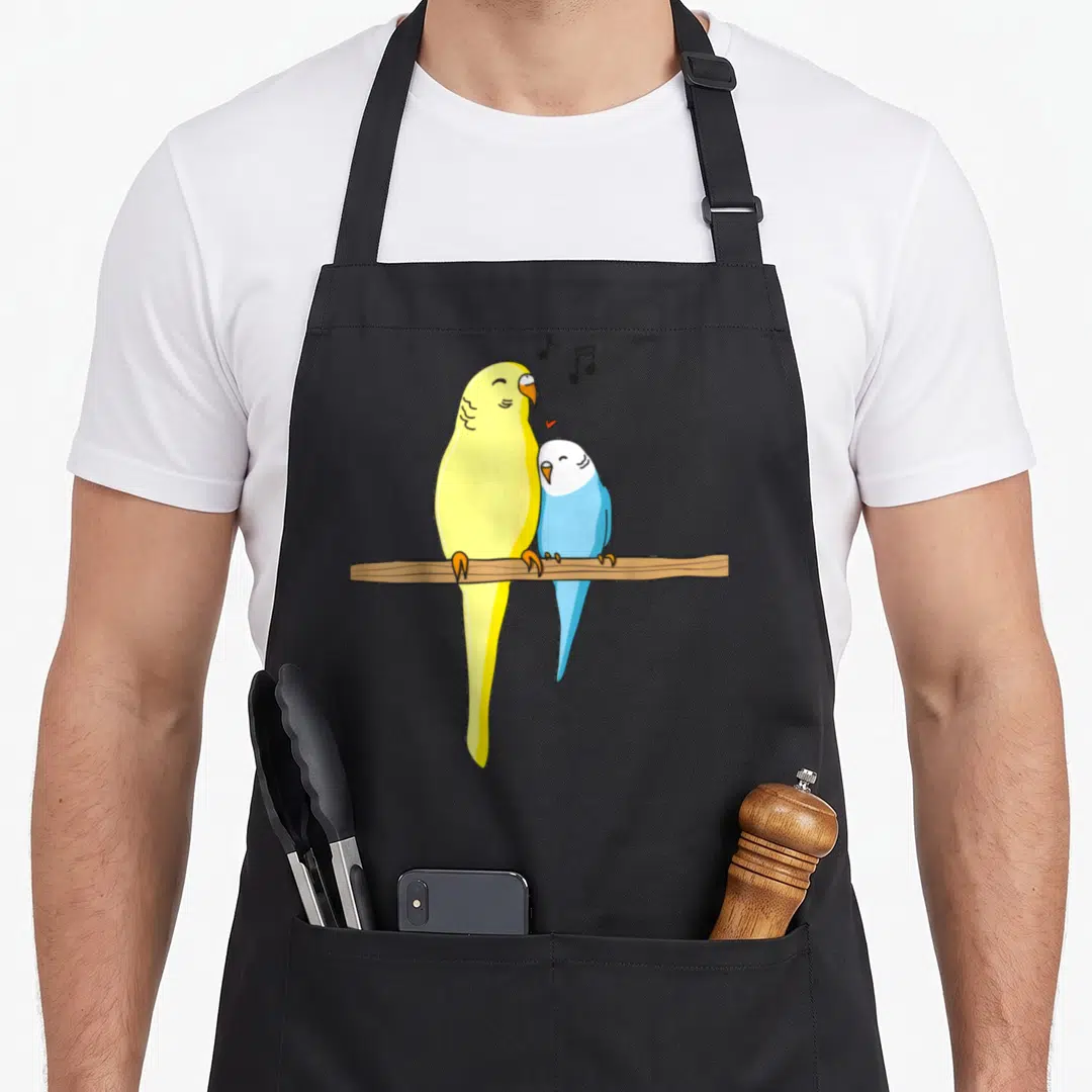 Familiy bird apron - Two cartoon parakeets perched on a brown branch with musical notes and a red heart — shown on a black cotton canvas apron against a white background