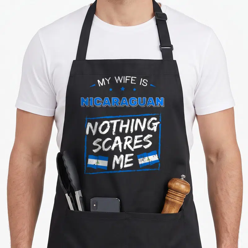 Nicaraguan wife apron - Blue and white stacked text reading My Wife is Nicaraguan Nothing Scares Me with three stars — shown on a black cotton canvas apron against a white background