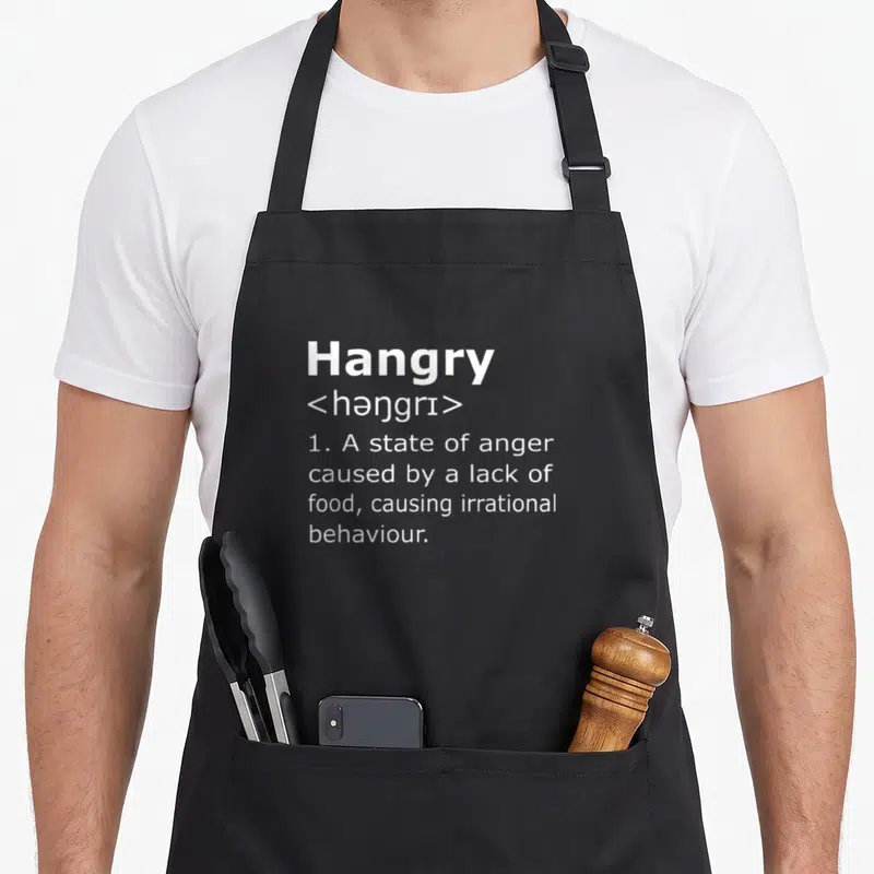 Definition hangry apron - White dictionary definition of Hangry printed on a black background — shown on a black cotton canvas apron against a white background