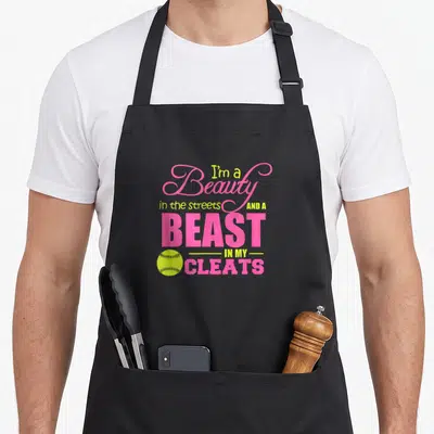 Beast beauty apron - Pink and yellow stacked text with a yellow softball graphic — shown on a black cotton canvas apron against a white background
