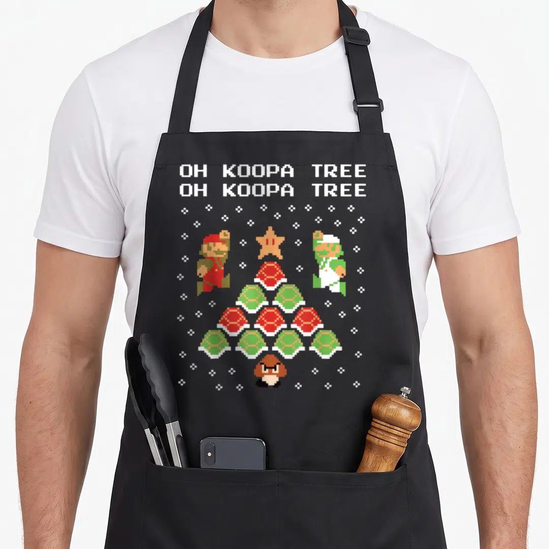 Koopa christmas tree apron - Pixel art Koopa shell tree with Mario Luigi and OH KOOPA TREE text — shown on a black cotton canvas apron against a white background