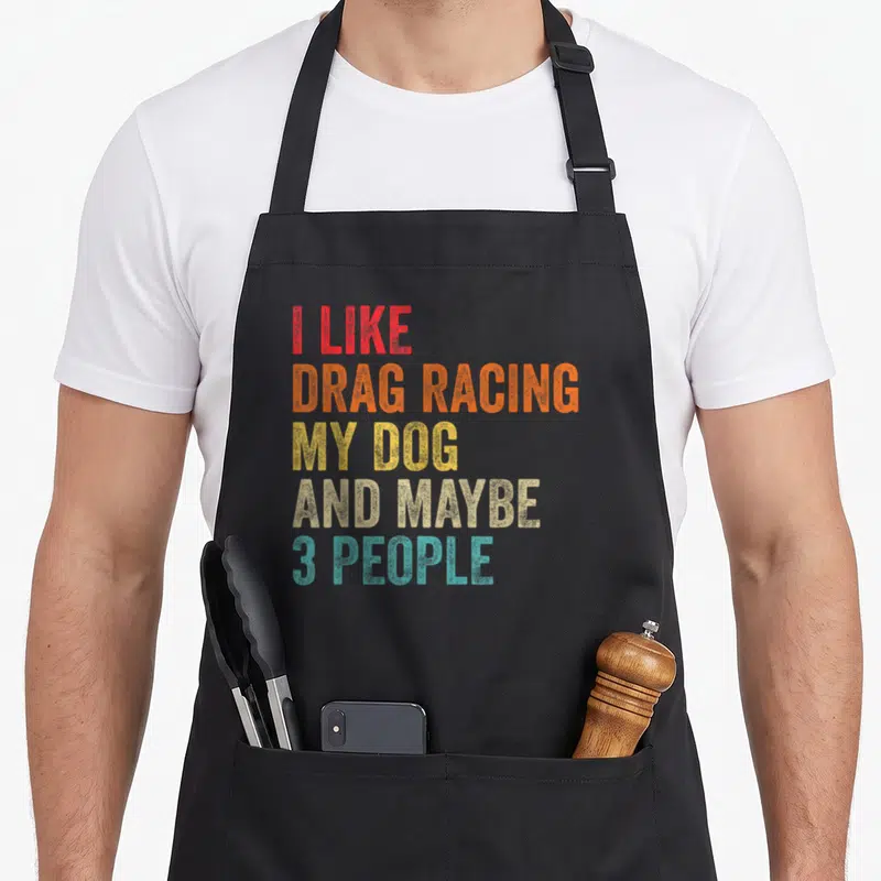 Drag dog apron - Stacked colorful distressed text reading I like drag racing my dog and maybe 3 people — shown on a black cotton canvas apron against a white background