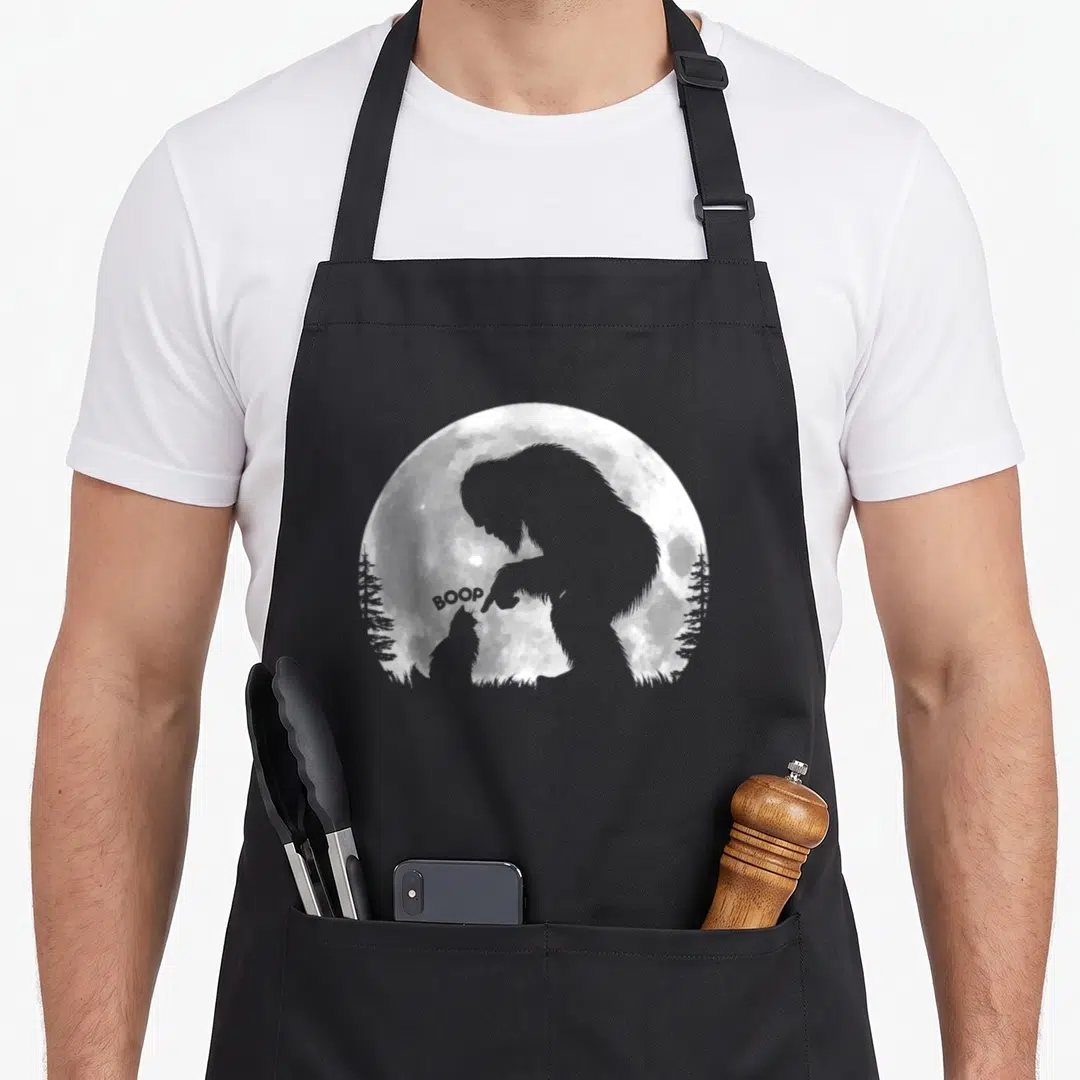 Hand cat apron - Grey Bigfoot silhouette booping a cat nose with BOOP text under a full moon — shown on a black cotton canvas apron against a white background