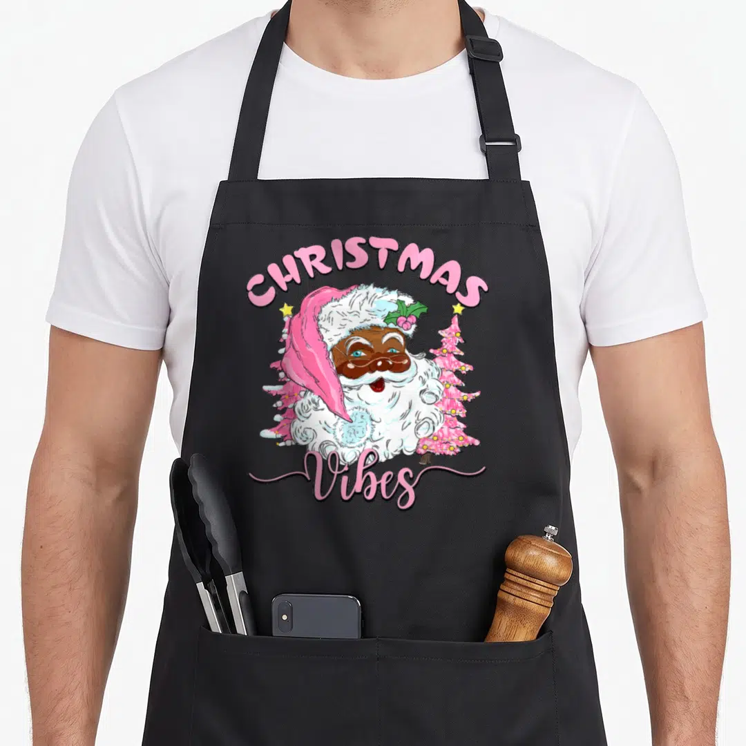 Holiday santa claus apron - Cartoon Santa with pink trees and arched CHRISTMAS Vibes text — shown on a black cotton canvas apron against a white background