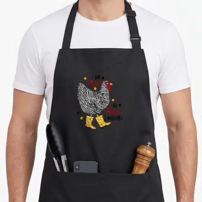 Fowl chicken with apron - Cartoon chicken in patterned boots with stars and text I Am Fluent IN Fowl LANGUAGE — shown on a black cotton canvas apron against a white background
