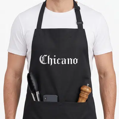 Chicano spanish aprons - White gothic typography spelling Chicano on grey background — shown on a black cotton canvas apron against a white background