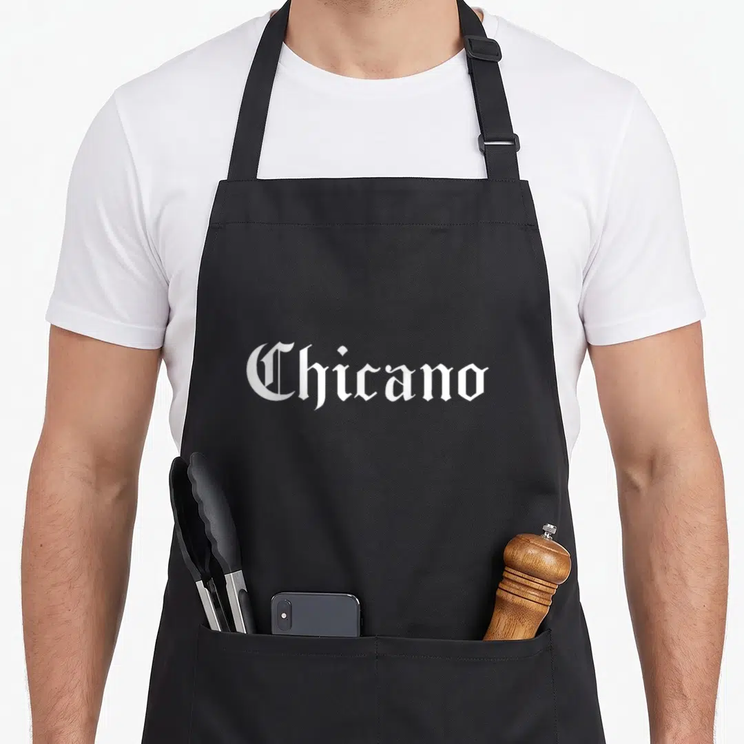 Chicano spanish aprons - White gothic typography spelling Chicano on grey background — shown on a black cotton canvas apron against a white background