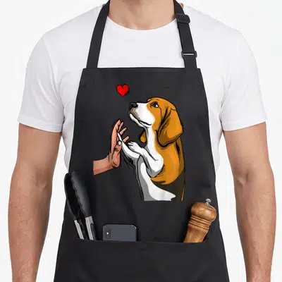 Retro dog beagle apron - Cartoon beagle facing left touching human hand under red heart, brown white peach colors — shown on a black cotton canvas apron against a white background
