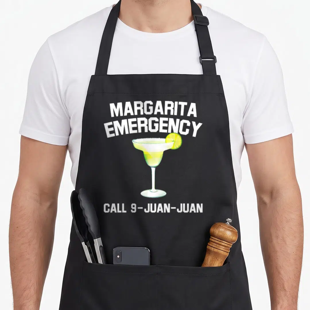 Margarita mexican apron - Cartoon margarita glass with lime slice and text MARGARITA EMERGENCY CALL 9-JUAN-JUAN — shown on a black cotton canvas apron against a white background