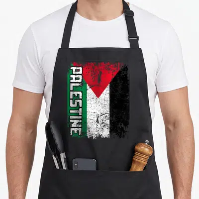 Funny flag palestine apron - Vertical PALESTINE text over distressed red black white and green flag graphic — shown on a black cotton canvas apron against a white background