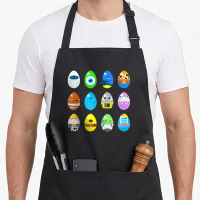 Character easter egg apron - Twelve colorful cartoon eggs in a grid pattern with character details like cow print — shown on a black cotton canvas apron against a white background