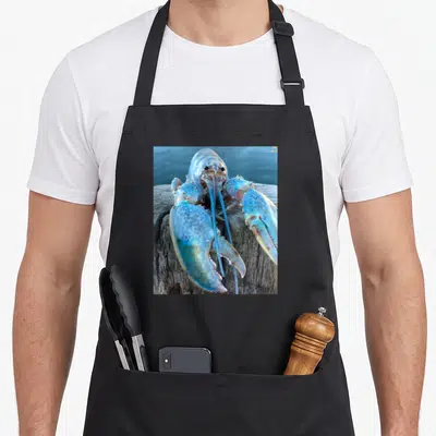 Jumpscare lobster apron - Rare blue lobster perched on weathered wooden post in realistic photo style — shown on a black cotton canvas apron against a white background