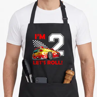 Toddler 2nd apron - Red yellow race car with I'M 2 LET'S ROLL text and checkered flag — shown on a black cotton canvas apron against a white background