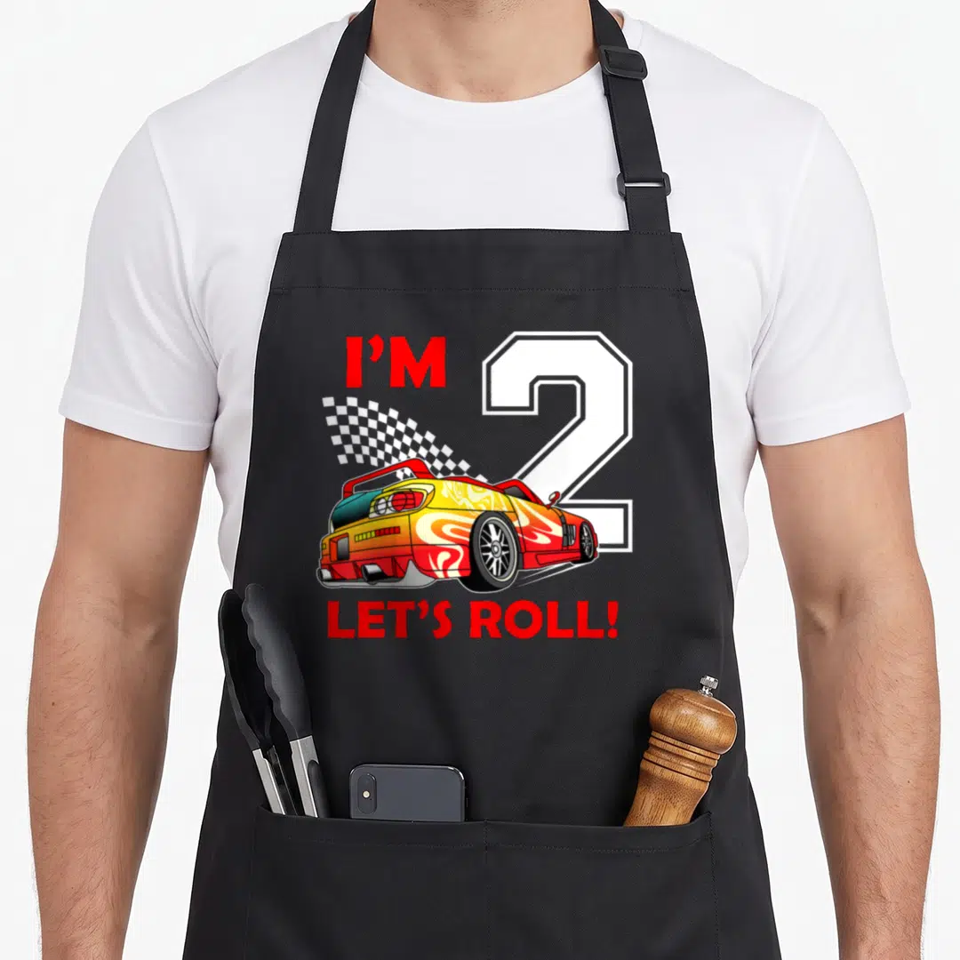 Toddler 2nd apron - Red yellow race car with I'M 2 LET'S ROLL text and checkered flag — shown on a black cotton canvas apron against a white background