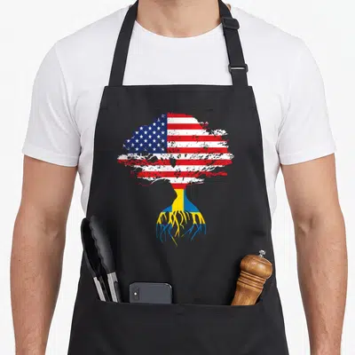Root swedish apron - Tree silhouette with US flag canopy and Swedish flag roots on black fabric — shown on a black cotton canvas apron against a white background