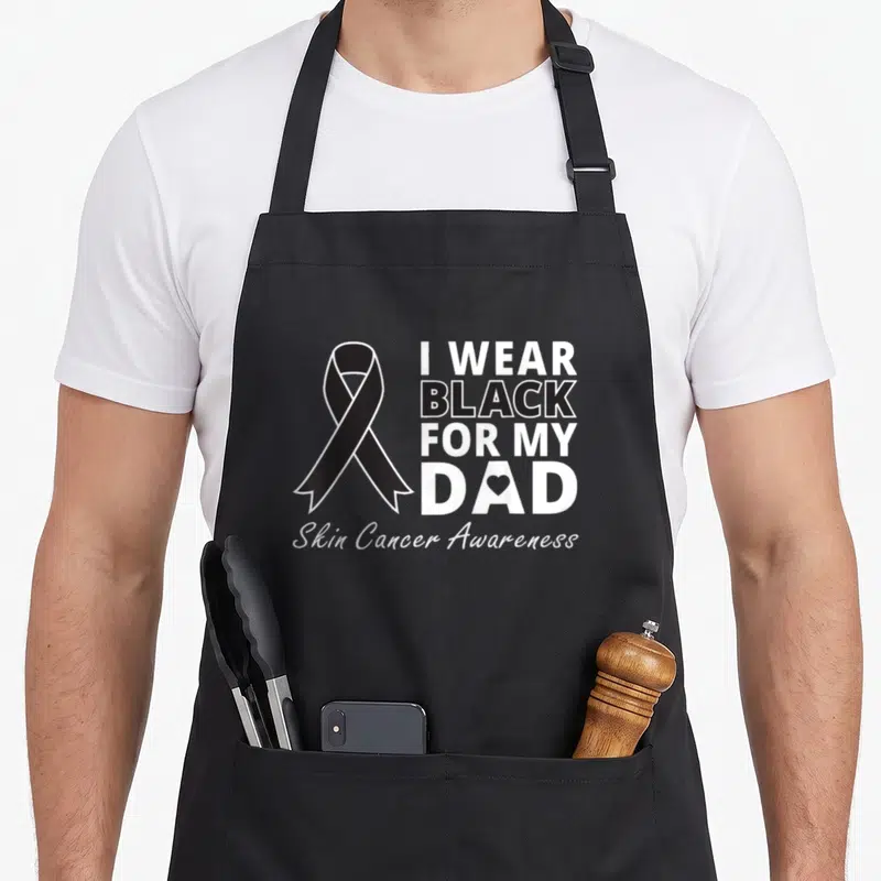 Funny warrior melanoma awareness apron - Black awareness ribbon next to stacked text I WEAR BLACK FOR MY DAD with heart — shown on a black cotton canvas apron against a white background
