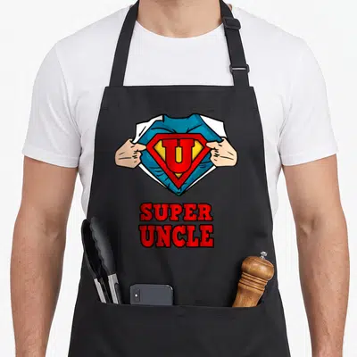 Uncle superhero apron - Cartoon hands revealing a U superhero emblem with stacked red SUPER UNCLE text below — shown on a black cotton canvas apron against a white background