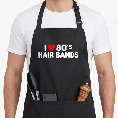 80s hair apron - White text reading I love 80s hair bands with a red heart symbol — shown on a black cotton canvas apron against a white background