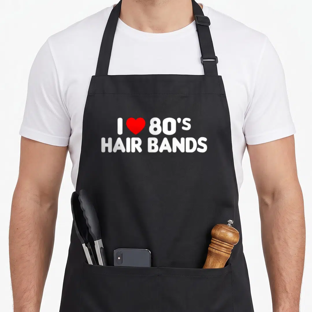 80s hair apron - White text reading I love 80s hair bands with a red heart symbol — shown on a black cotton canvas apron against a white background