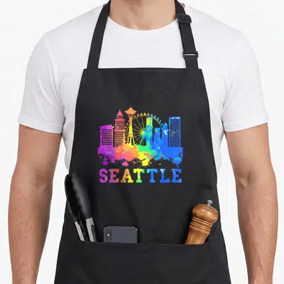 Watercolor seattle apron - Rainbow watercolor Seattle skyline with Ferris wheel and text SEATTLE below — shown on a black cotton canvas apron against a white background