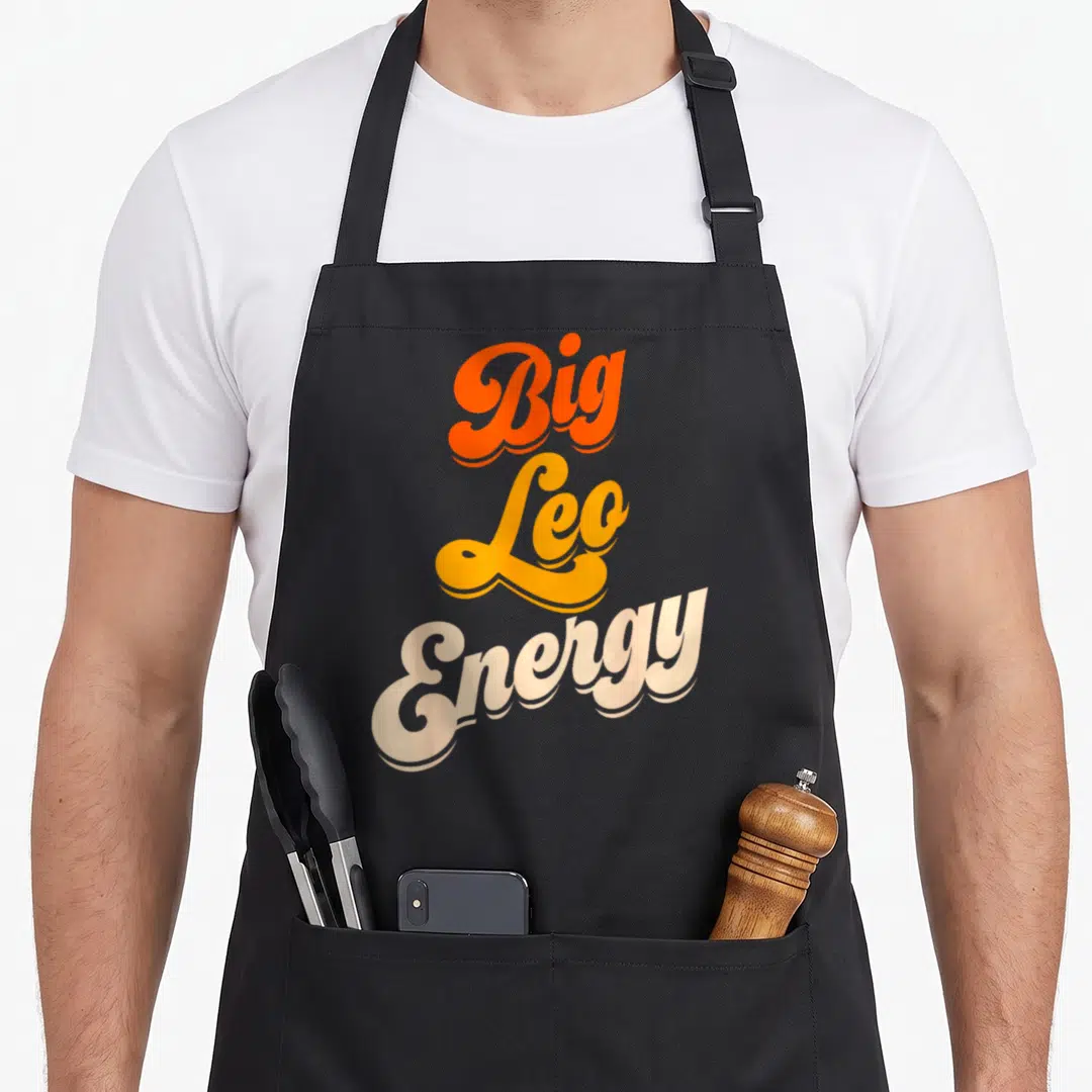 Energy leo apron - Stacked Big Leo Energy text in orange yellow and cream script — shown on a black cotton canvas apron against a white background