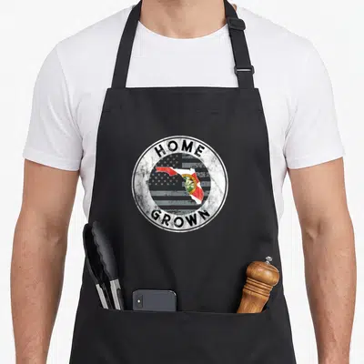 Florida american flag apron - Distressed circle with HOME GROWN text surrounding a Florida map filled with state flag — shown on a black cotton canvas apron against a white background