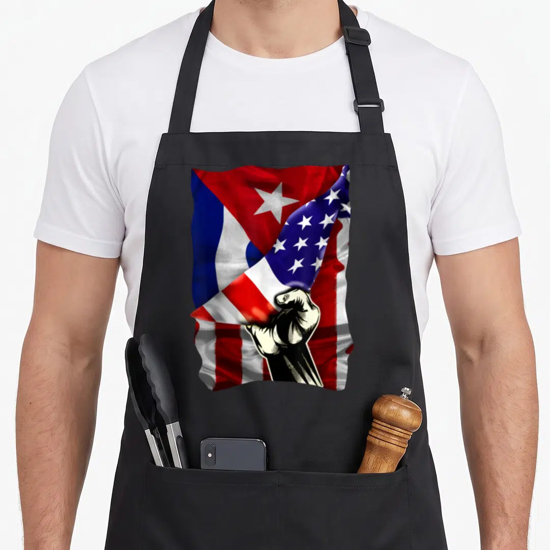 Cuban root cuba american flag apron - Clenched fist over merging Cuban and American flags in red white blue and black — shown on a black cotton canvas apron against a white background