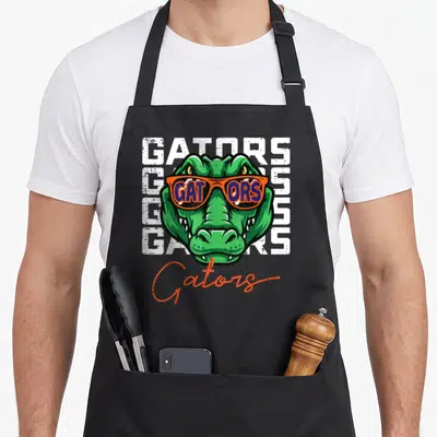 Sunglass youth apron - Green alligator head in orange sunglasses over stacked white GATORS text and script logo — shown on a black cotton canvas apron against a white background