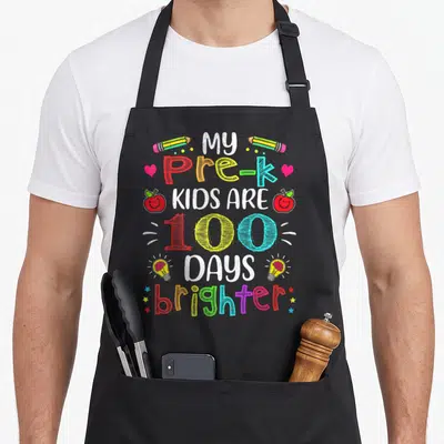 Brighter teacher apron - My Pre-K Kids Are 100 Days Brighter text with pencils, apples, and lightbulbs — shown on a black cotton canvas apron against a white background