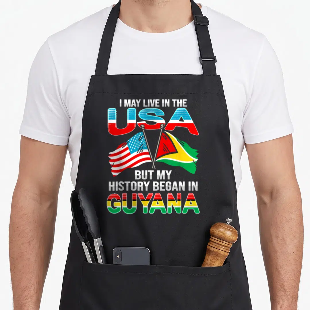 Proud guyana apron - Crossed US and Guyana flags with text I MAY LIVE IN THE USA BUT MY HISTORY BEGAN IN GUYANA — shown on a black cotton canvas apron against a white background