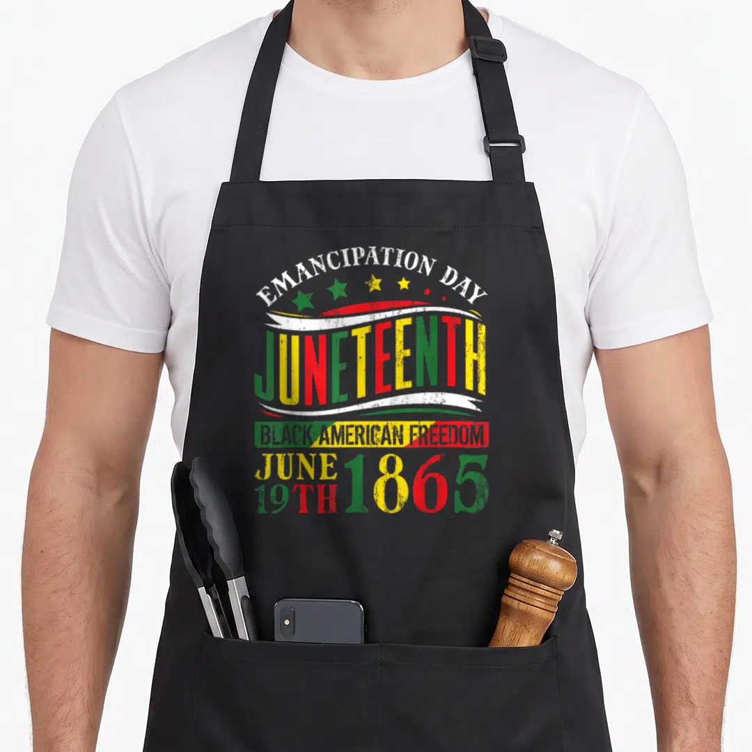 Freedom african apron - Juneteenth text with stars and ribbons in red yellow green and white on black background — shown on a black cotton canvas apron against a white background