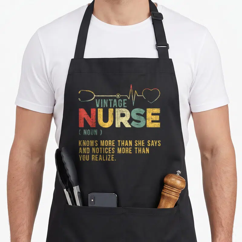 Definition nursing apron - Vintage nurse dictionary definition text with stethoscope and heartbeat line in olive green — shown on a black cotton canvas apron against a white background
