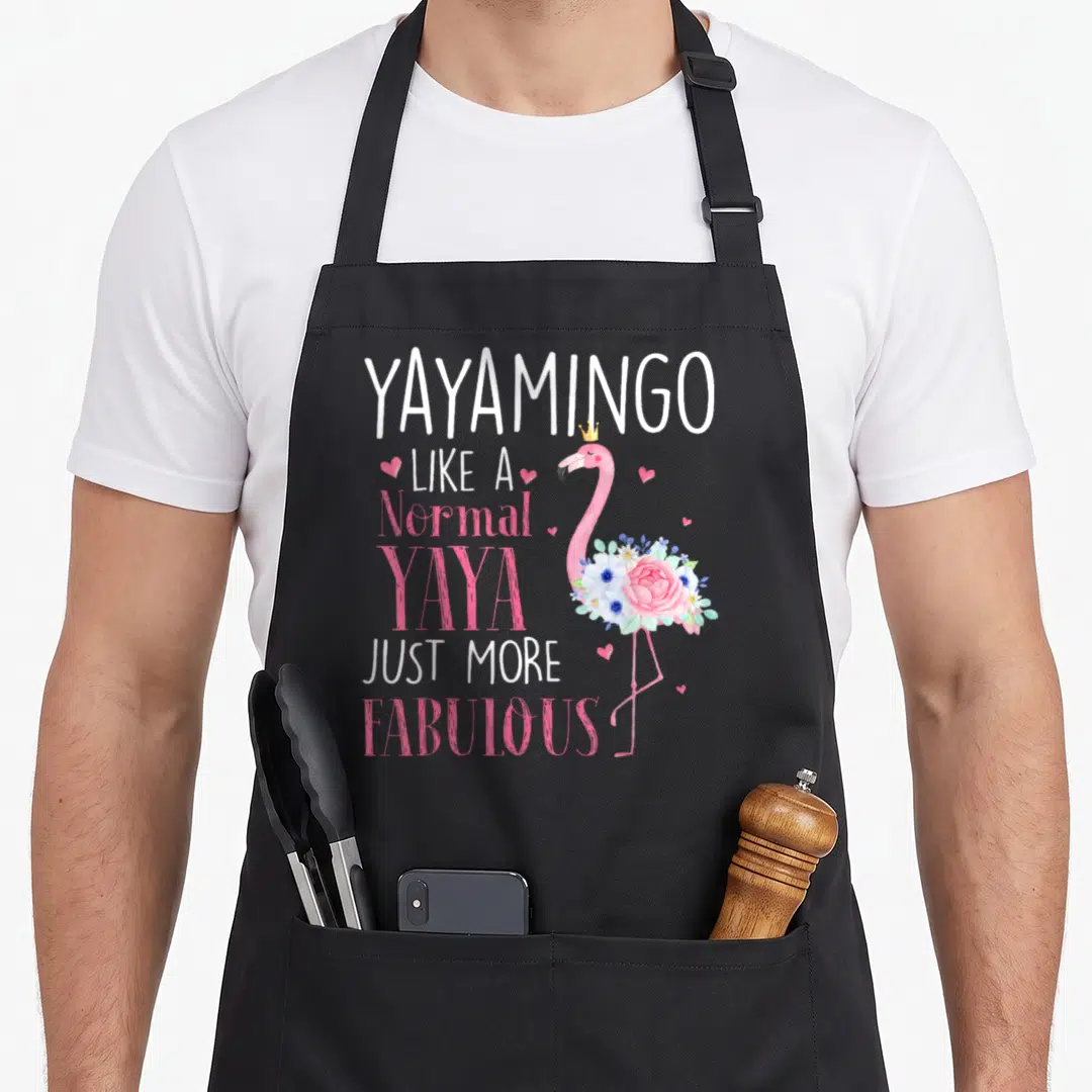 Yayamingo grandma apron - Pink flamingo with crown and flowers next to Yayamingo text — shown on a black cotton canvas apron against a white background